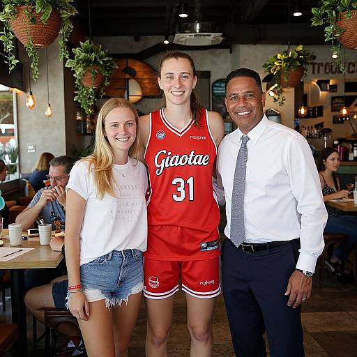 Photograph of a smiling young woman in denim shorts and white top, a tall woman in a red Gatorade basketball jersey, and a man in