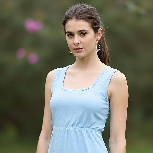 Photograph of a young woman with fair skin, dark brown hair in a ponytail, wearing a light blue sleeveless dress and silver earrings, standing