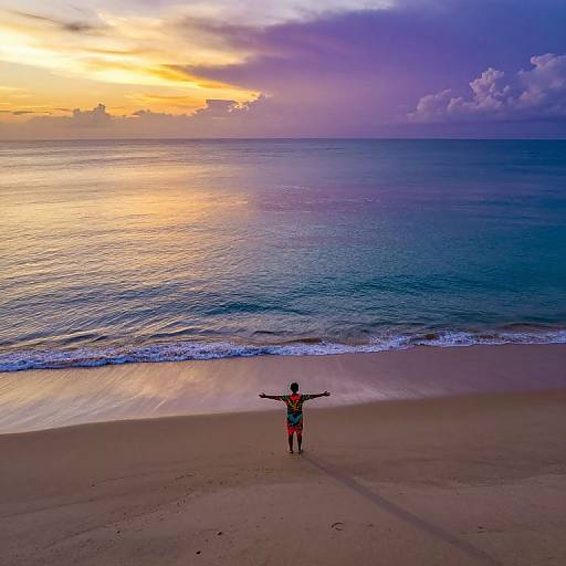 Photograph of a person with arms outstretched, standing on a sandy beach at sunset, facing a vibrant, colorful ocean horizon.