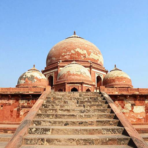 Photograph of a weathered red and white domed Mughal mausoleum with a wide, stone staircase leading up to the central dome