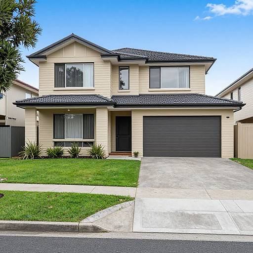 Photograph of a modern two-story beige house with black roof, large windows, black garage door, and neatly manicured lawn.