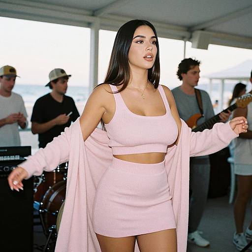 Photograph of a young woman with long black hair, wearing a pink ribbed crop top and mini skirt, light pink open cardigan, standing confidently