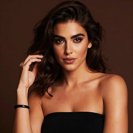 Photograph of a beautiful woman with wavy dark hair, olive skin, and intense brown eyes, wearing a strapless black top, against a dark