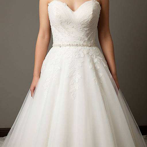 Photograph of a woman in a strapless, white lace wedding dress with a sweetheart neckline and full, tulle skirt, standing against a gray background