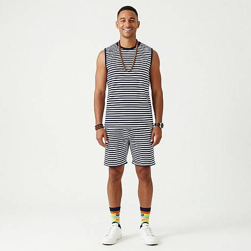 Photograph of a smiling young man with short dark hair, wearing a black and white striped sleeveless shirt and shorts, white sneakers, and yellow-striped