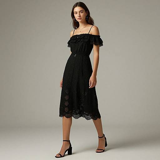 Photograph of a young woman with long brown hair, wearing an off-shoulder, black lace dress and black high-heeled sandals, standing against