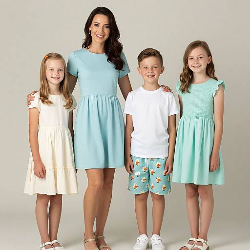 Photograph of a smiling woman in a light blue dress, flanked by three children in white, blue, and light blue dresses, and white and