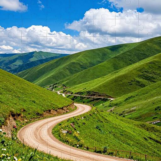 Photograph of a winding dirt road through lush green hills under a bright blue sky with scattered white clouds.