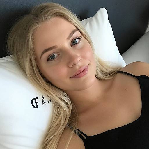 Photograph of a blonde woman with blue eyes, wearing a black top, lying on a white pillow with black text, smiling softly.