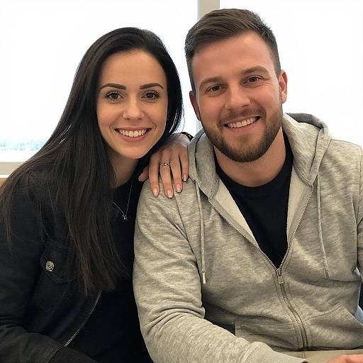 Photograph of a smiling couple; woman with long black hair, black jacket, and man with short brown hair, beard, gray hoodie.