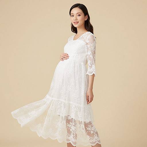 Photograph of a pregnant Asian woman with long black hair, wearing a flowing white lace dress, standing against a beige background.