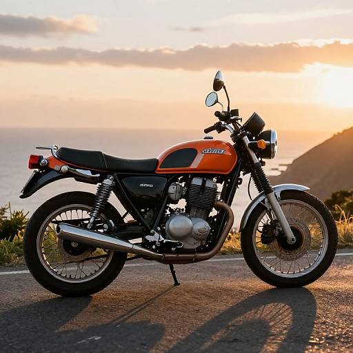 Photograph of a vintage orange Suzuki motorcycle with black seat and chrome exhaust, parked on a coastal road at sunset.