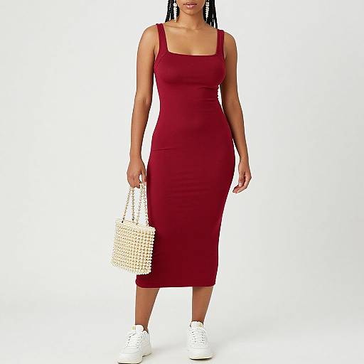 Photograph of a woman with dark skin, wearing a sleeveless, form-fitting, red midi dress, white sneakers, and holding a white,