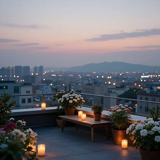 Photograph of a rooftop at twilight, featuring a wooden bench with potted flowers, lit candles, and a cityscape view.