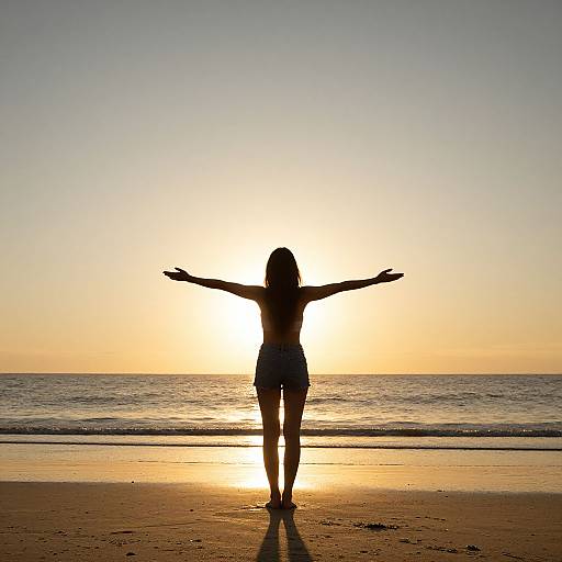 Photograph of a silhouetted woman with outstretched arms standing on a beach at sunset, with the sun directly behind her, ocean in