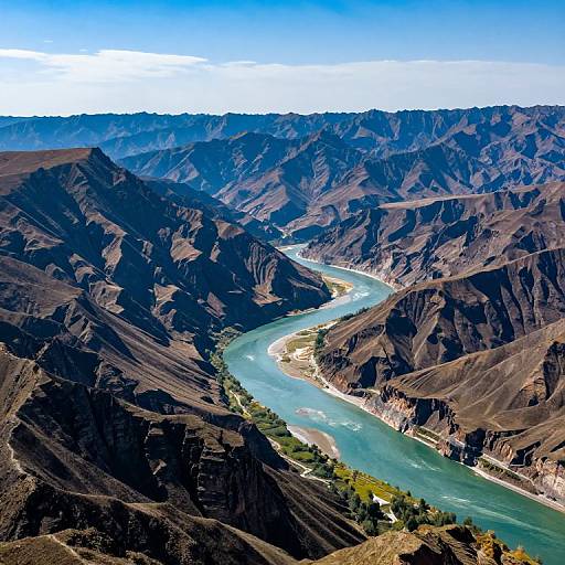 Photograph of a winding turquoise river cutting through rugged, brown, mountainous terrain under a bright blue sky with sparse clouds.