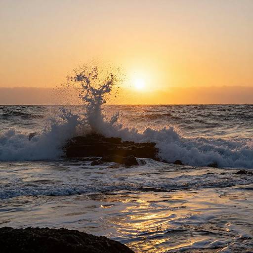 Photograph of a sunset over the ocean, with a large wave splashing against a rocky outcrop, reflecting golden sunlight on the water.