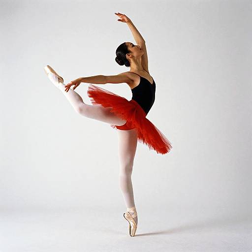 Photograph of a graceful ballerina in a black leotard and red tutu, poised on pointe, with an elegant arm raise against
