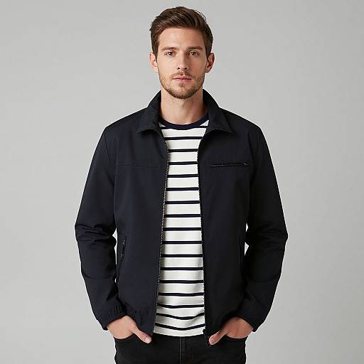 Photograph of a handsome, young, white man with short brown hair, beard, wearing a black jacket over a white, black-striped shirt, hands