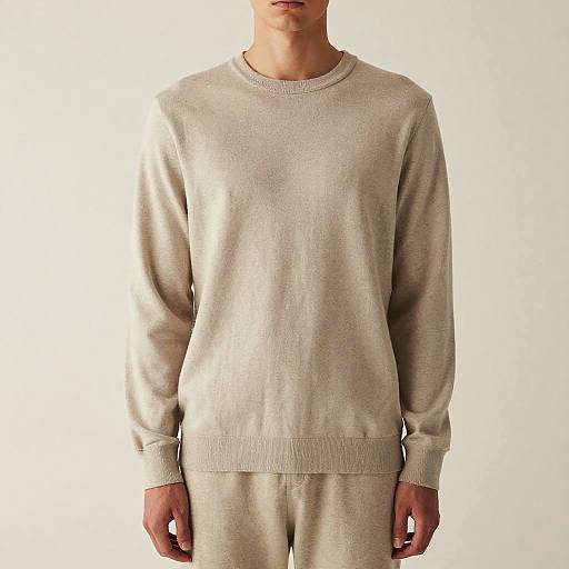 Photograph of a man from neck to waist, wearing a light beige, long-sleeve sweater and matching sweatpants, against a plain white background