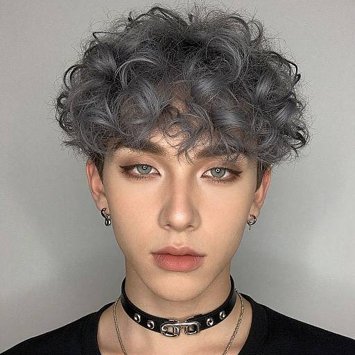 Photograph of androgynous person with short, curly, gray-black hair, light skin, green eyes, black choker, earrings, black