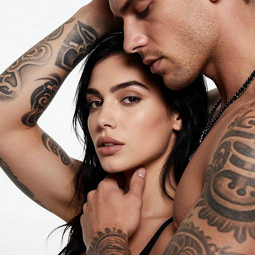 Tattooed, muscular man with short hair embraces a beautiful woman with long black hair and light skin, his hand gently holding her neck. Photograph