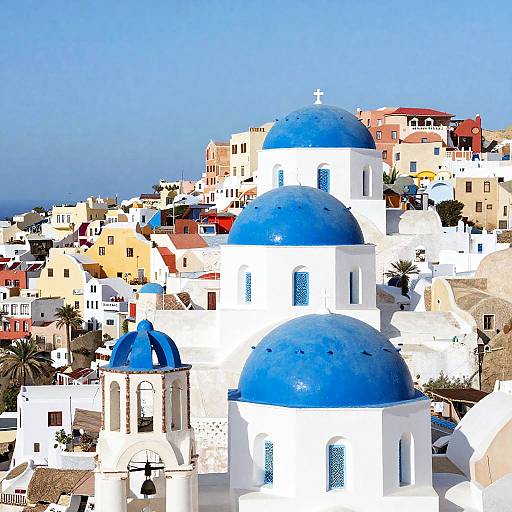 Photograph of a vibrant Greek island village featuring white-washed buildings with bright blue domes, set against a clear blue sky.