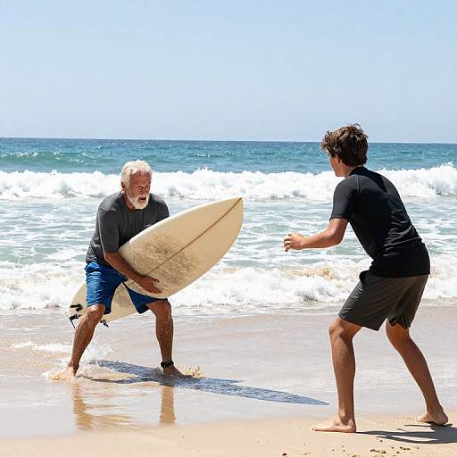 Photograph of an older white man with gray beard and blue shorts holding a surfboard facing a younger man in black shirt and gray shorts on a sunny