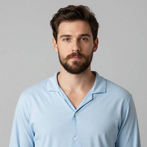 Photograph of a bearded man with short dark hair, wearing a light blue polo shirt, against a plain white background.