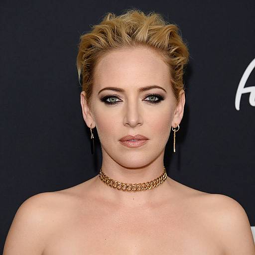 Photograph of a fair-skinned woman with blonde, voluminous updo, blue eyes, dark eyeliner, nude lips, gold chain necklace,