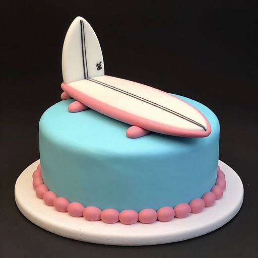 Photograph of a blue cake with pink spheres, topped with a white surfboard-shaped fondant decoration and pink accents, on a white base.
