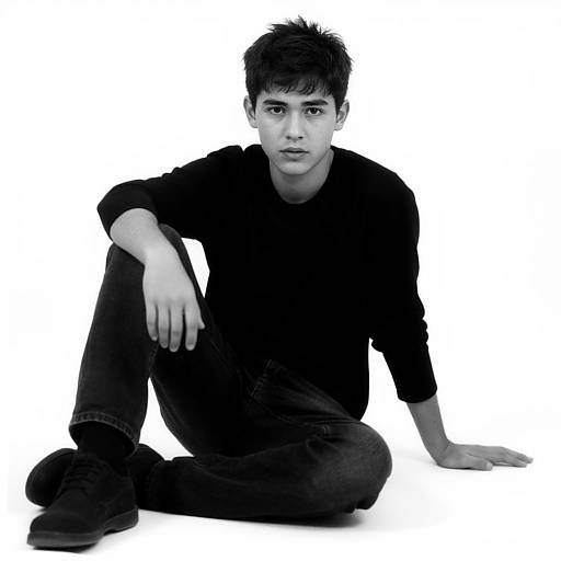 Black-and-white photograph of a young Asian man with short, dark hair, wearing a black long-sleeve shirt and jeans, sitting on the ground