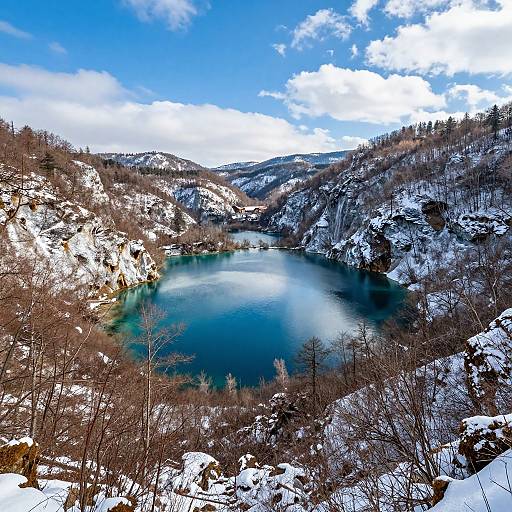 Photograph of a snow-covered mountainous landscape with a vivid blue, partially frozen lake in the center under a bright blue sky.