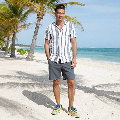 Photograph of a smiling, fit man with short brown hair, wearing a white striped shirt, gray shorts, and yellow sneakers, standing on a sunny