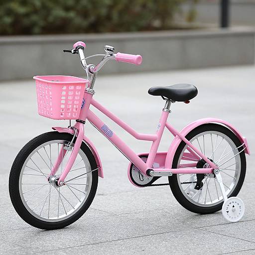 Photograph of a pink children's bicycle with a pink basket, black seat, and white wheels, parked on a paved sidewalk.