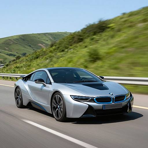 Photograph of a sleek, silver BMW sports car with black accents speeding down a mountain road with green hills in the background.