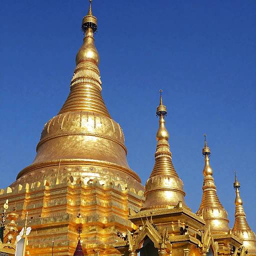 Photograph of golden Buddhist stupas with intricate details, illuminated against a clear, vibrant blue sky, showcasing their ornate, glistening structures.