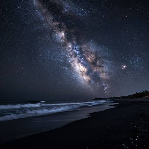 Photograph of a dark, starry night sky over a beach, with the Milky Way galaxy visible and waves crashing on the shore.