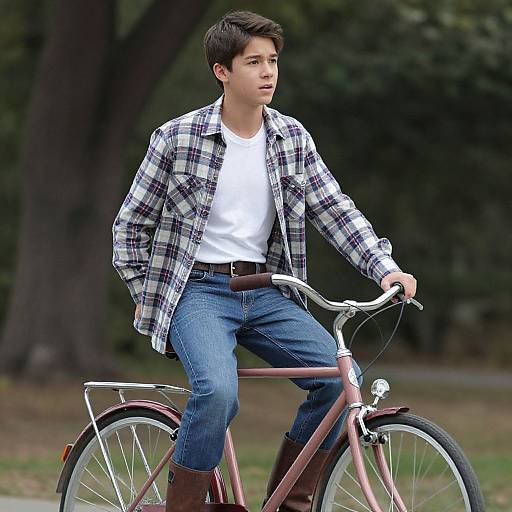 Young Asian man with short black hair, wearing a white t-shirt, plaid shirt, blue jeans, and brown boots, riding a pink bicycle in