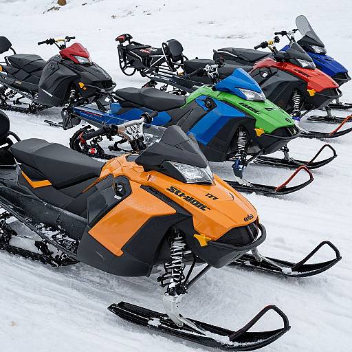 Photograph of six colorful snowmobiles parked in a snowy field, featuring bright orange, blue, green, red, and black colors. Snowy