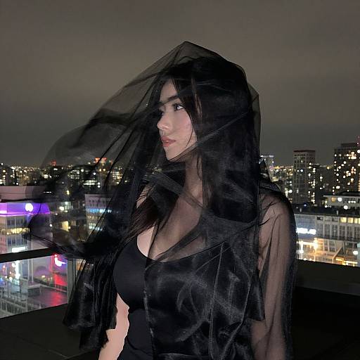Photograph of a young woman with long black hair, wearing a sheer black top, standing on a rooftop at night, with a cityscape and illuminated