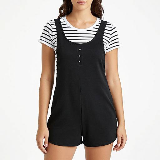 Photograph of a woman wearing a black pinafore dress over a white and black striped short-sleeve shirt, with a plain white background.