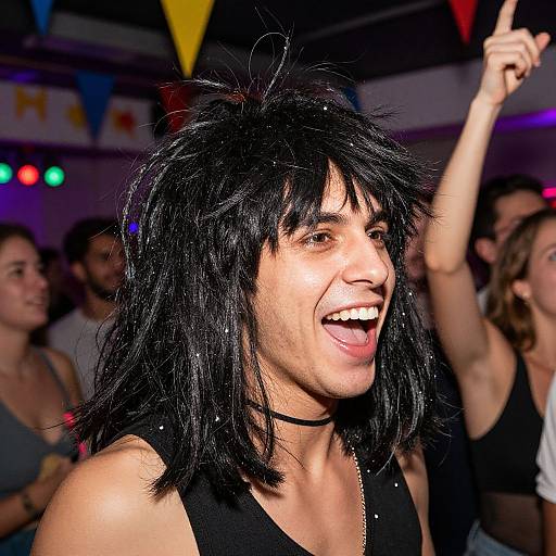 Photograph of a joyful woman with black, spiky hair, black tank top, and choker, raising her right hand, smiling widely at a