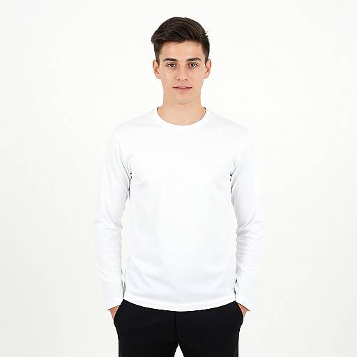 Photograph of a young man with short black hair, light skin, wearing a plain white long-sleeve shirt and black pants, standing against a