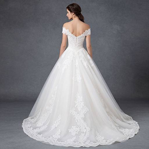 Photograph of a brunette woman in a white, off-shoulder lace wedding gown with a full skirt, facing away, against a gray textured background