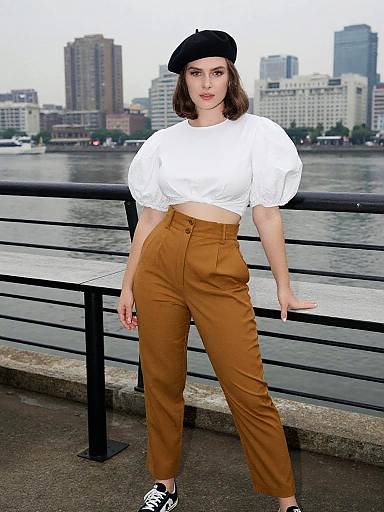 Photograph of a young woman with fair skin, dark wavy hair, black beret, white puffy-sleeve crop top, high-w