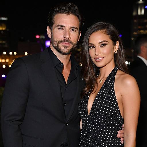 Photograph of a bearded man in a black suit and a woman with long dark hair in a black, sparkling halter dress, standing close together
