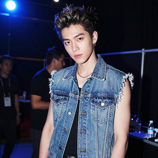 Photograph of a young Asian man with spiky black hair, wearing a frayed denim sleeveless vest, black shirt, and earring, under