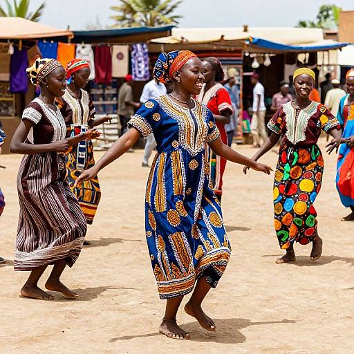 Photograph of African women dancing in colorful traditional dresses with bold patterns, standing on sandy ground, market stalls and people in background.