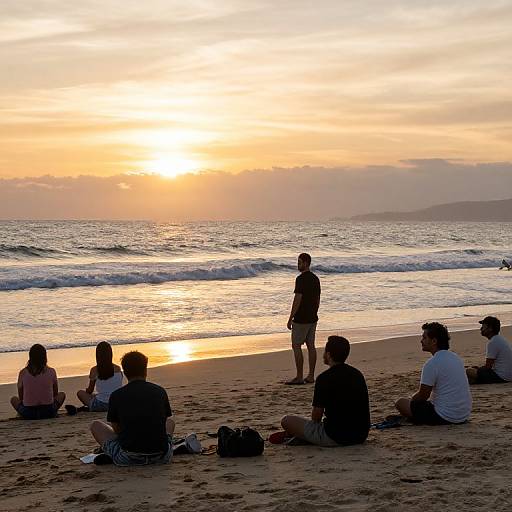 Photograph of a serene beach at sunset, with six people sitting or standing on the sand, watching the sun set over the ocean.
